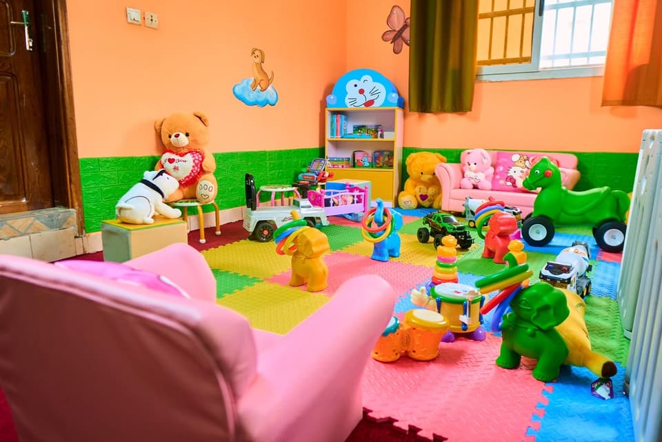 Un coin calme avec une petite bibliothèque garnie de livres, un fauteuil rose, des peluches et un tapis de sol matelassé.