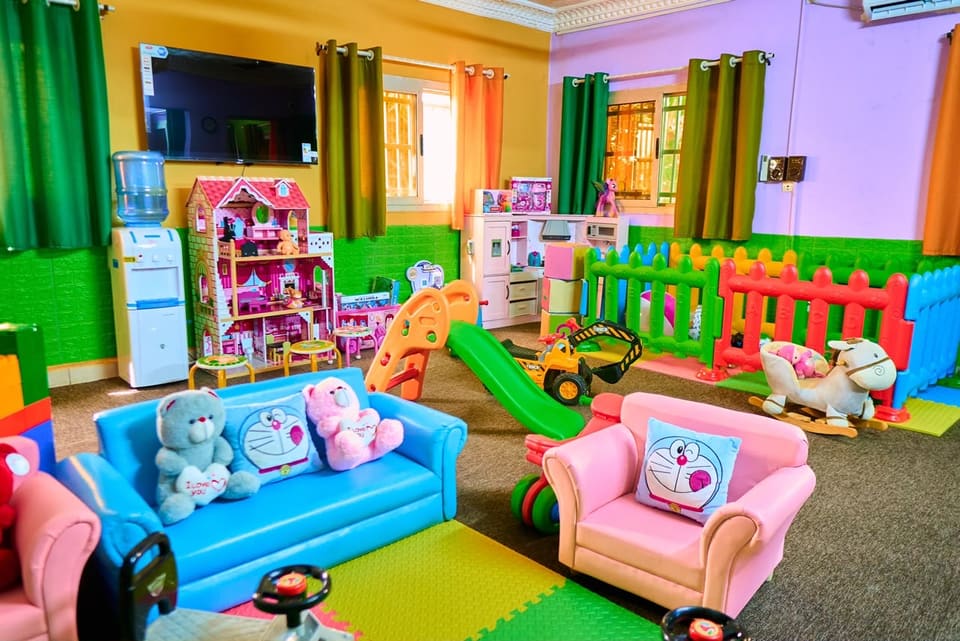 L’espace crèche : petits canapés, maison de poupée, cuisine d’imitation et coin délimité par une barrière colorée.